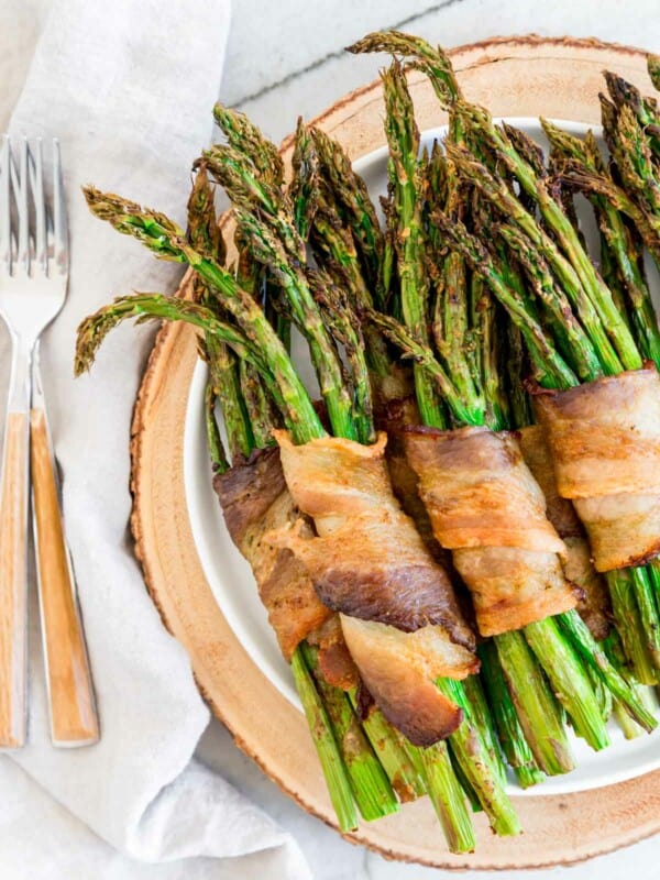 Air fried asparagus bunches wrapped in crispy bacon on a plate with forks to the side.
