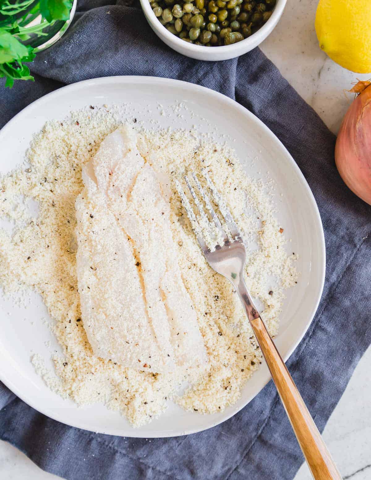 Dredging cod filet in almond flour on a plate.