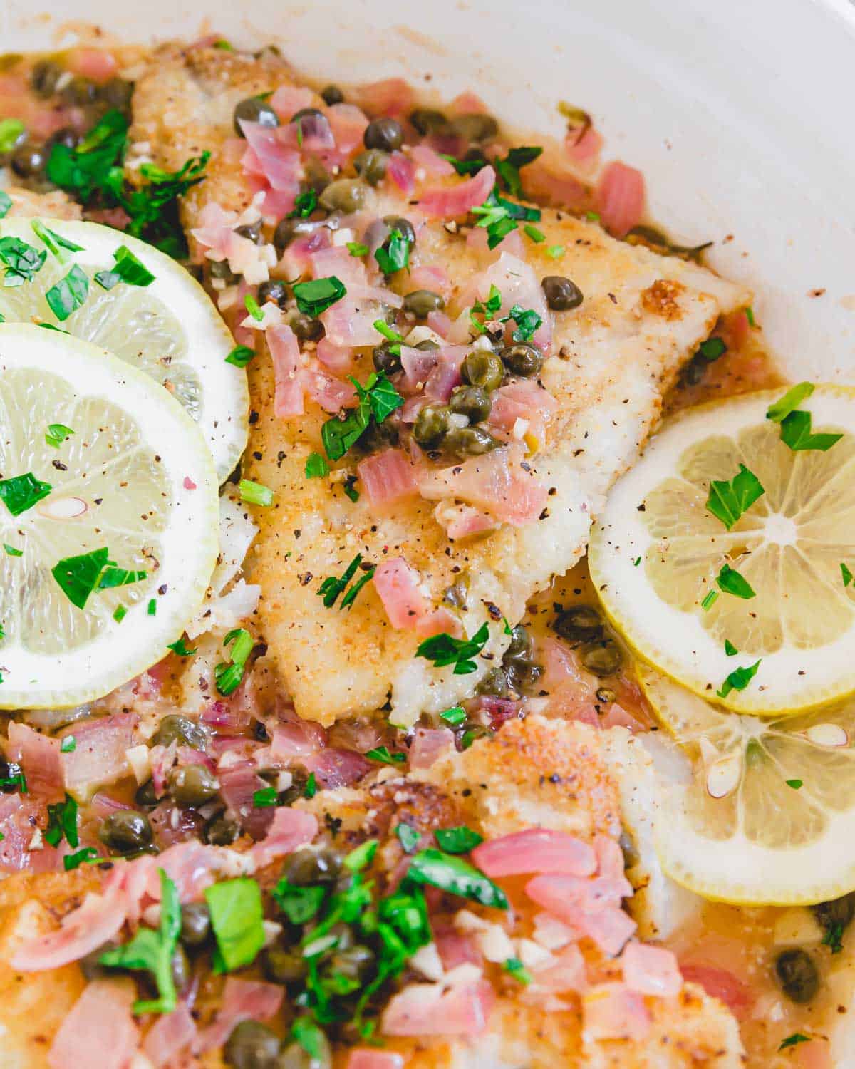 Close up of cod piccata in a white skillet.