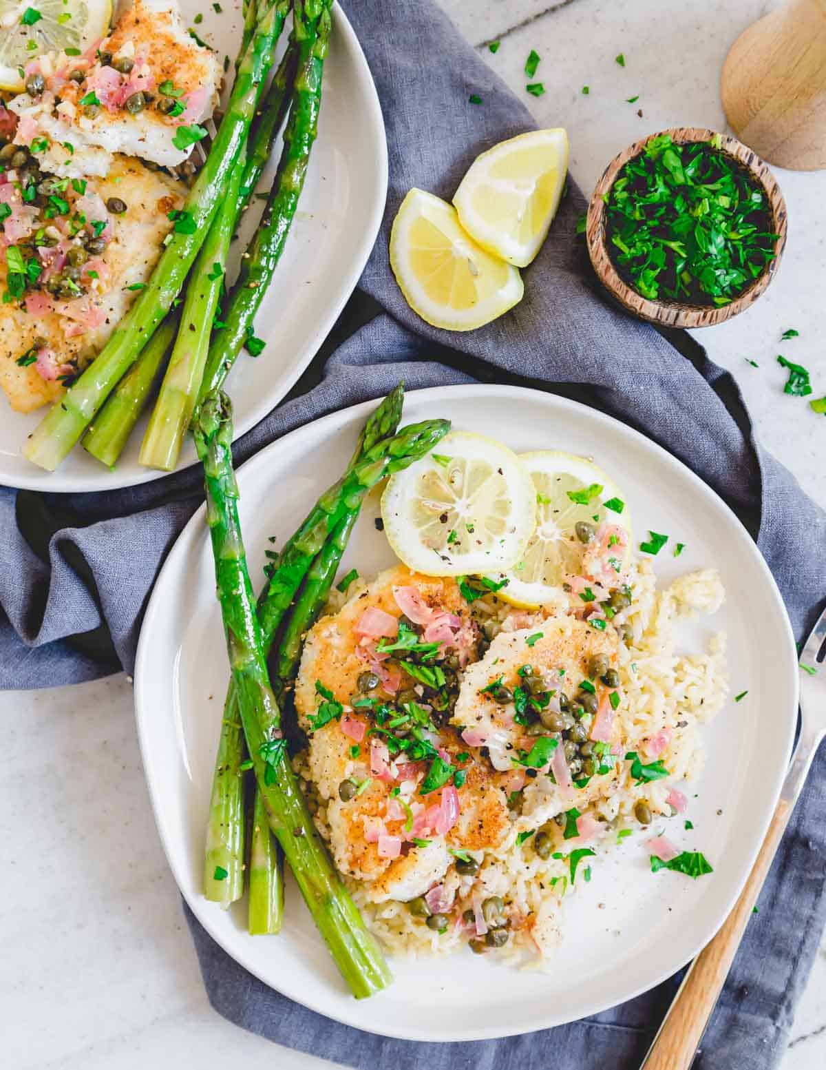 Overhead shot of cod piccata on plates with rice and asparagus.