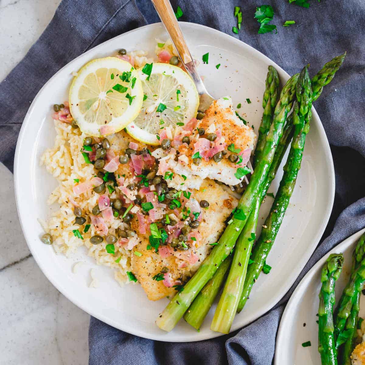 Cod piccata on a plate with lemon slices, rice and asparagus.