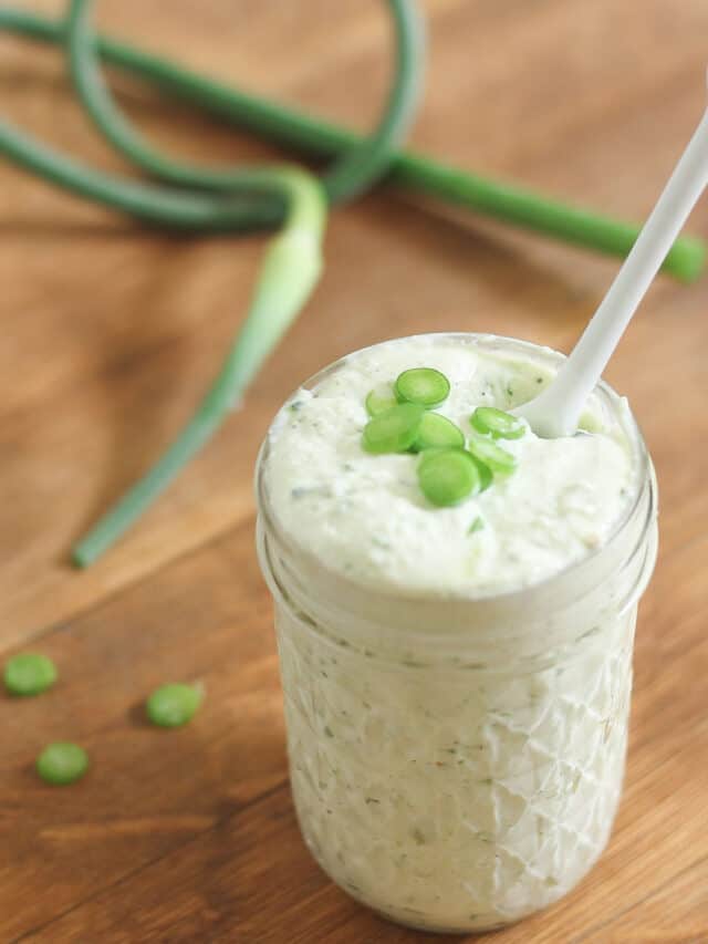 Garlic scape pesto in a jar with a white spoon.