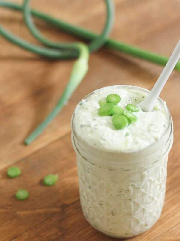 Garlic scape pesto in a jar with a white spoon.