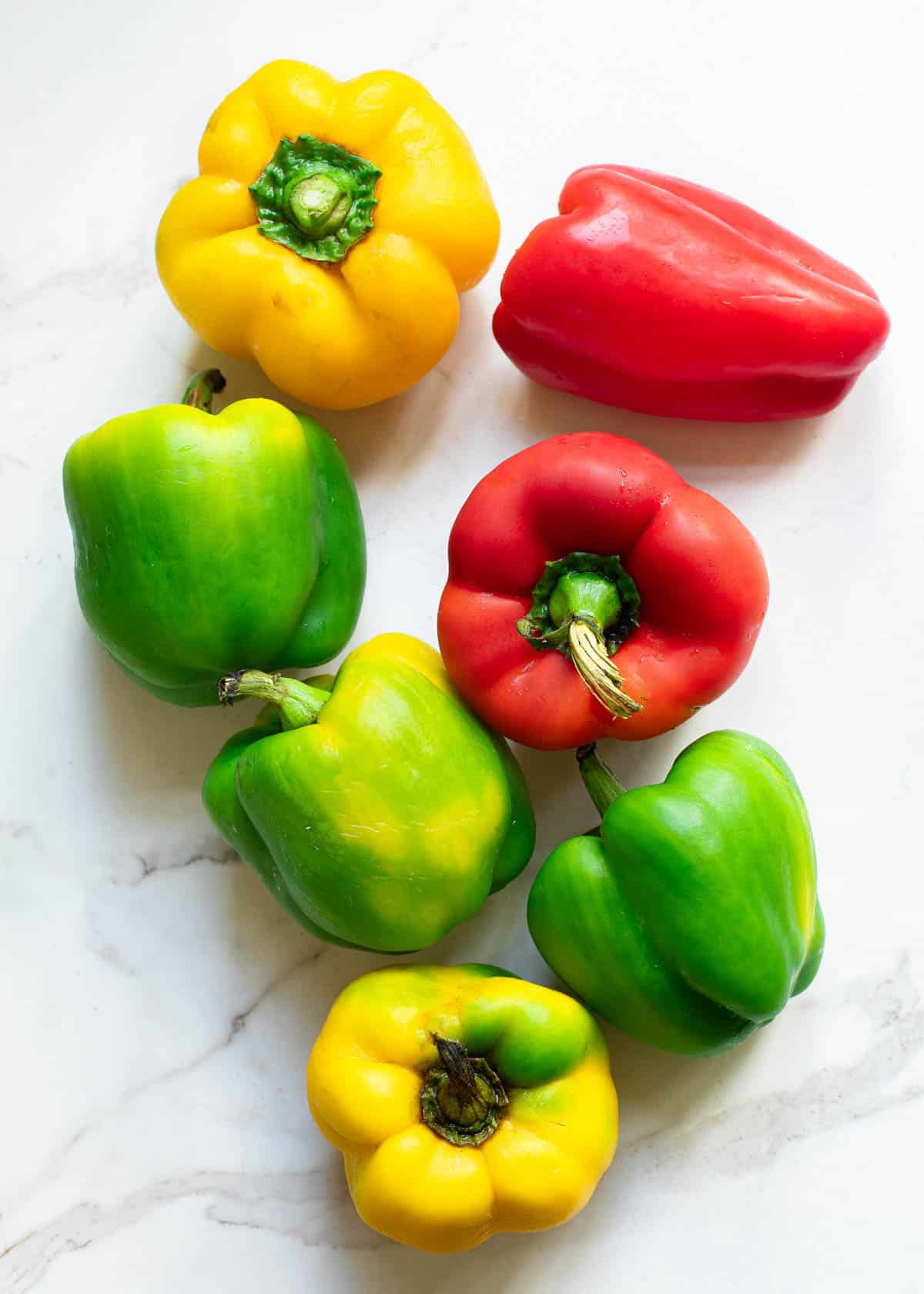 Assorted colors of bell peppers on a marble surface.