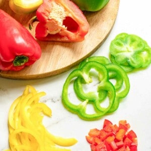 Different color bell peppers cut in a variety of ways on a white marble surface.