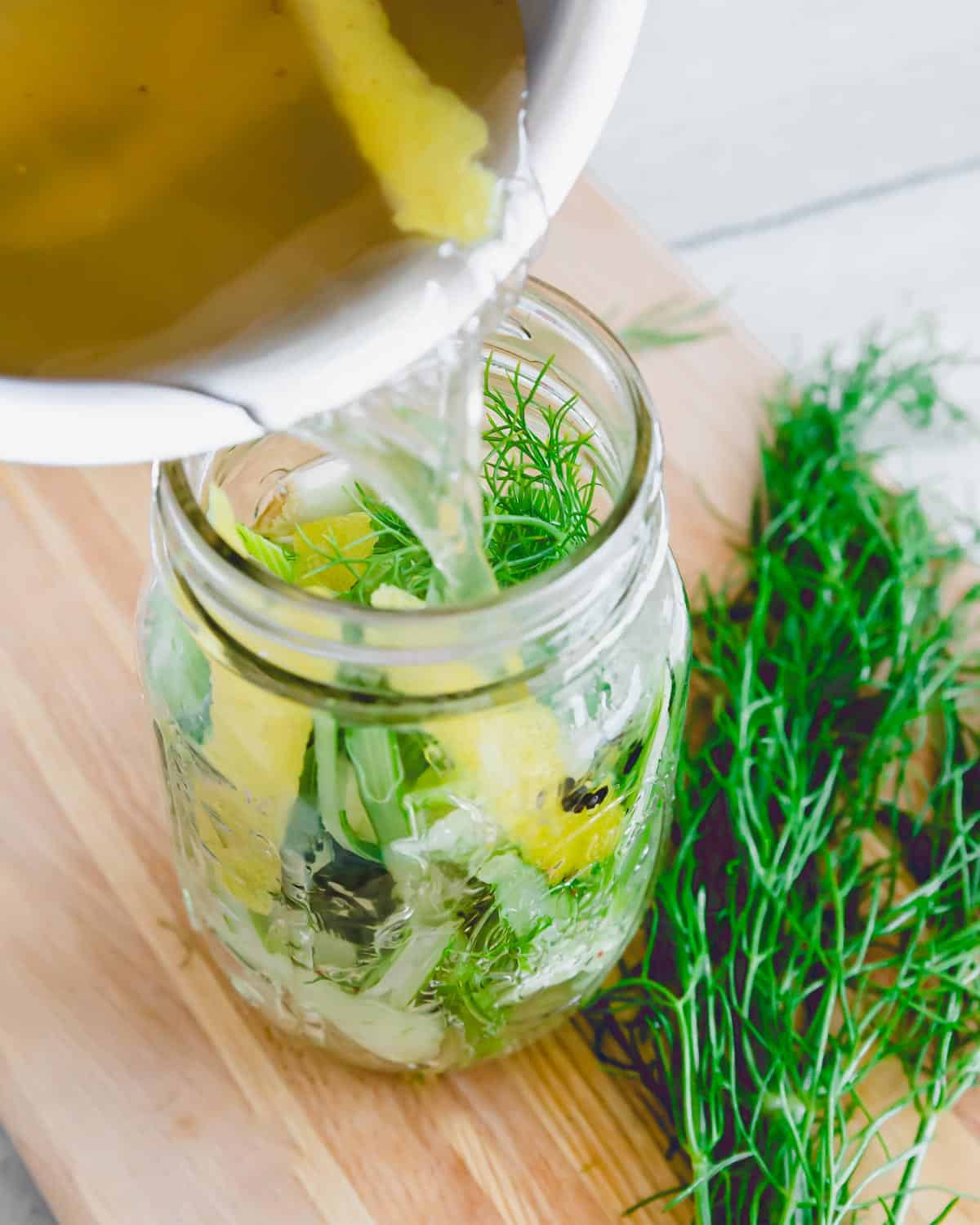 Pouring pickling liquid into a mason jar with fennel.