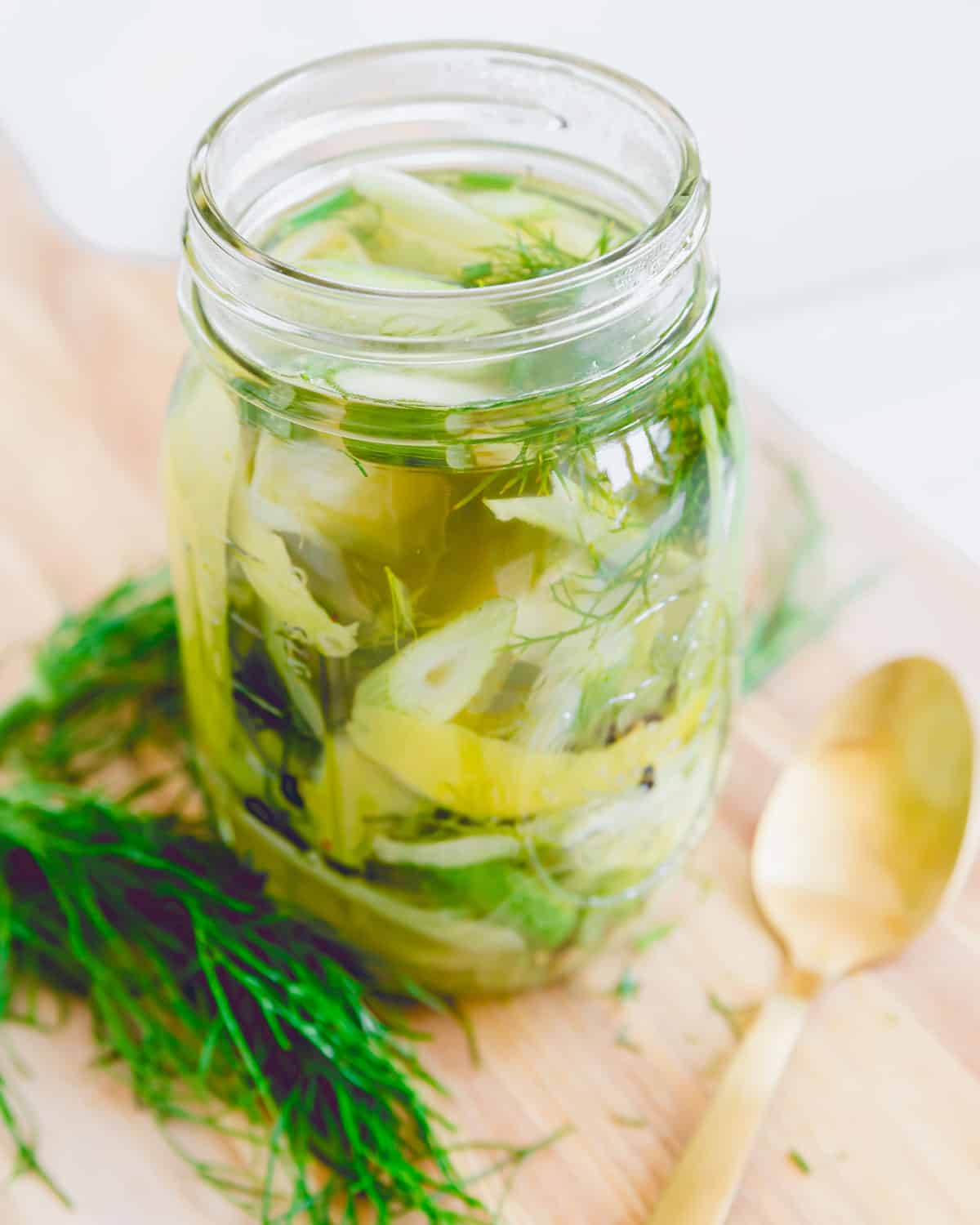 Pickled fennel in a glass mason jar on a cutting board.