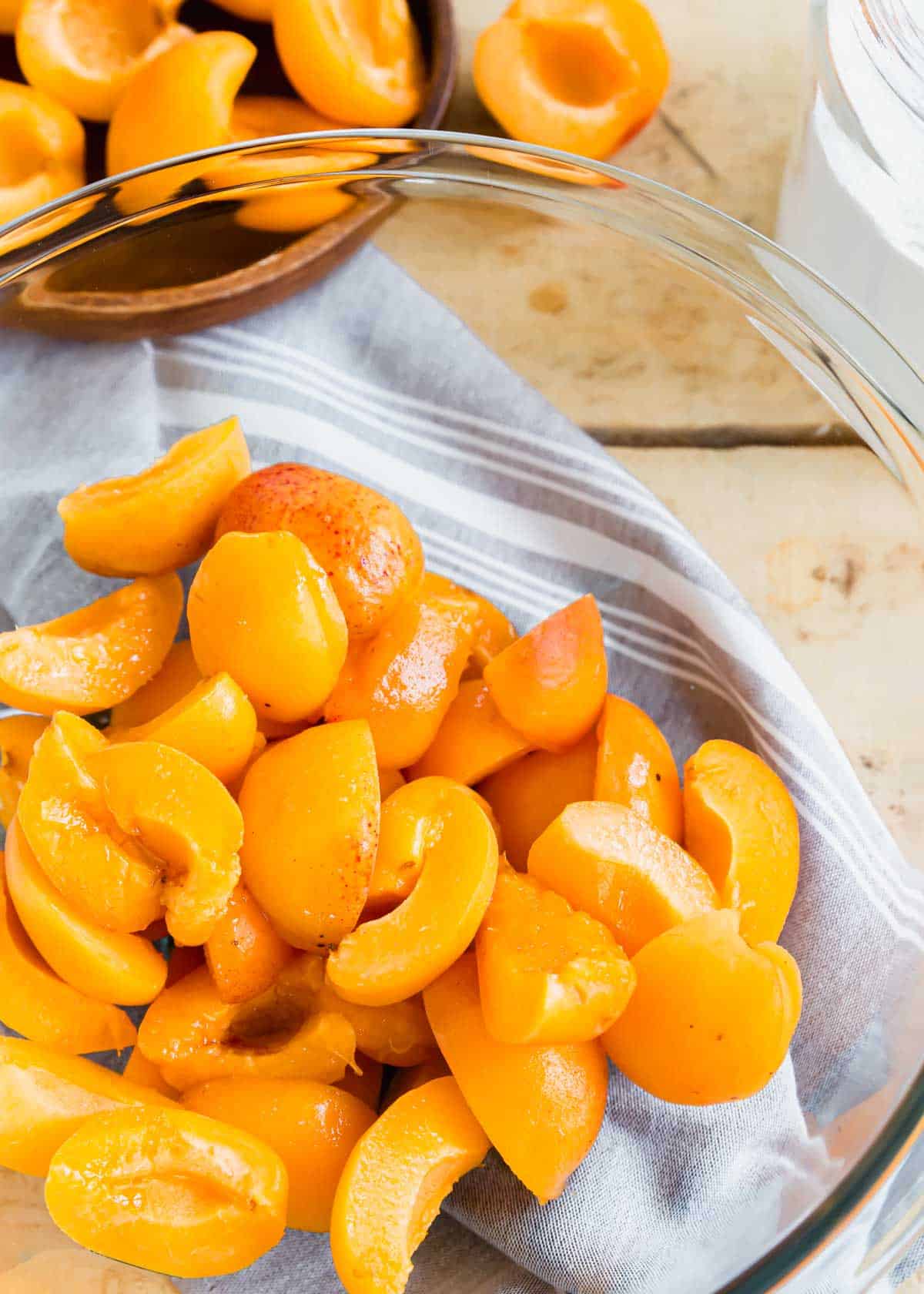 Apricot quarters in a glass bowl with a kitchen towel underneath.