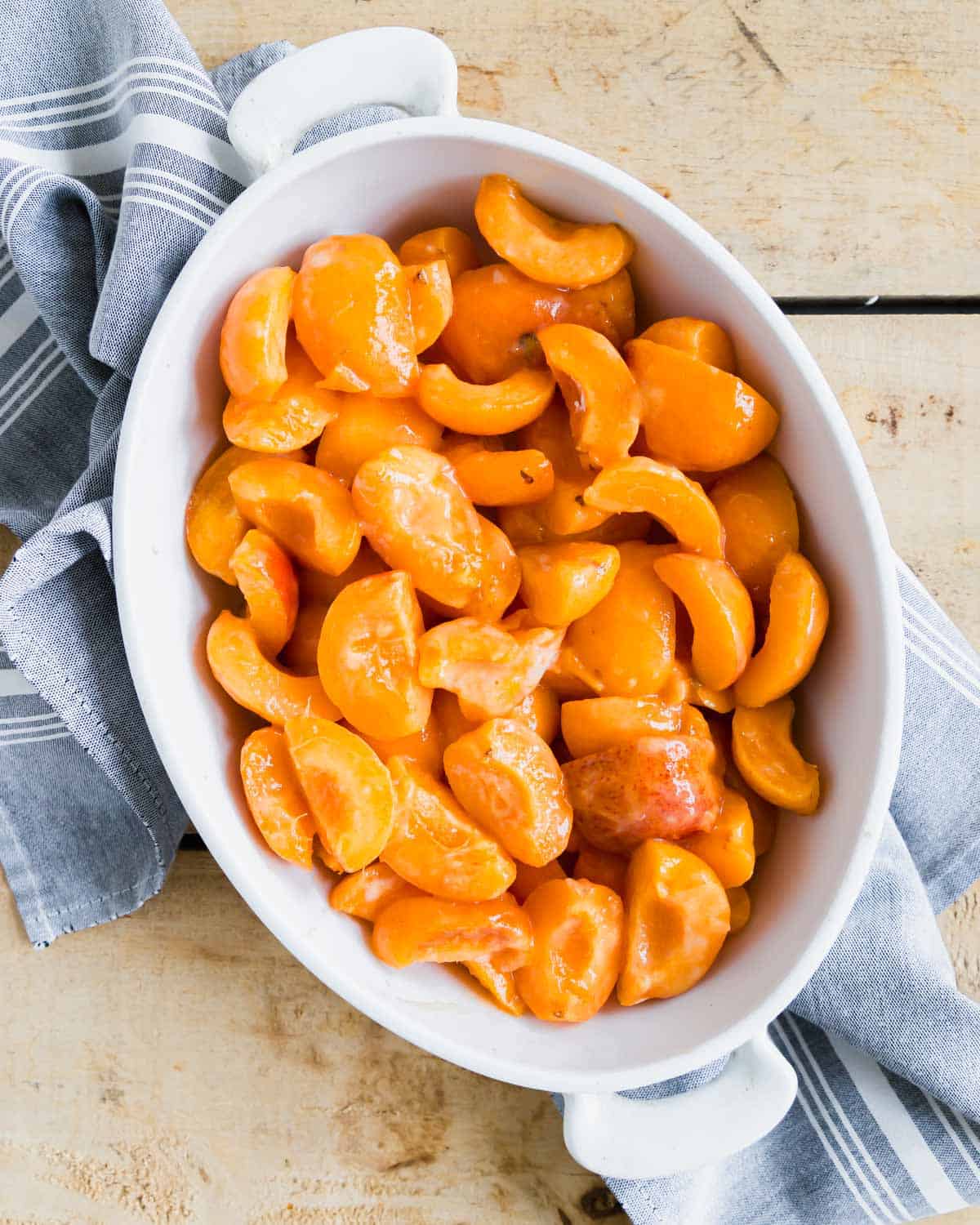 Apricots in a white baking dish with a gray and white striped linen beneath.