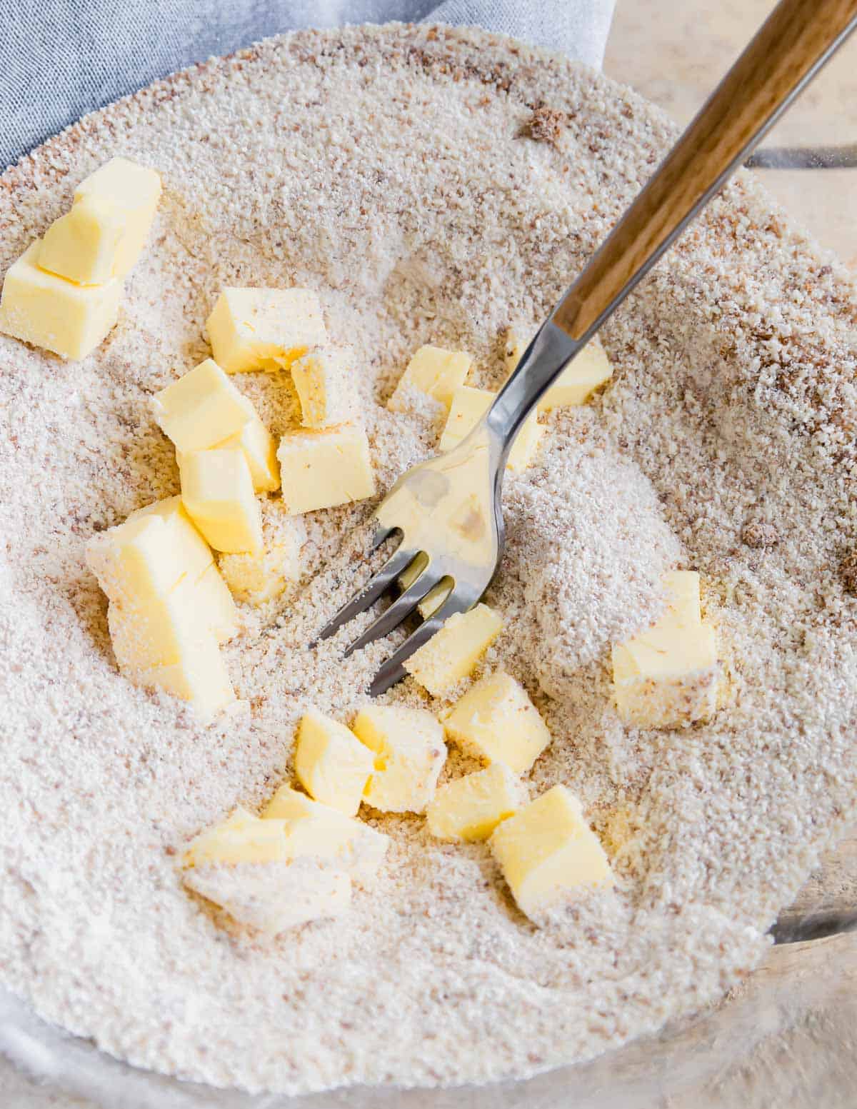 Cutting cold butter cubes into flour mixture in a glass bowl with a fork.