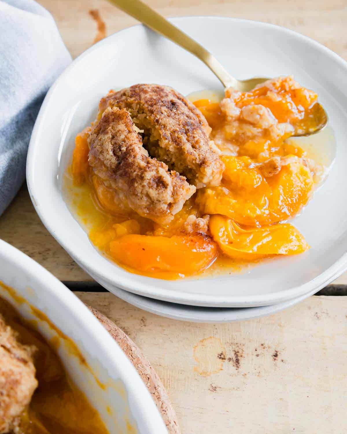 Apricot cobbler portion on two stacked plates with gold spoon.