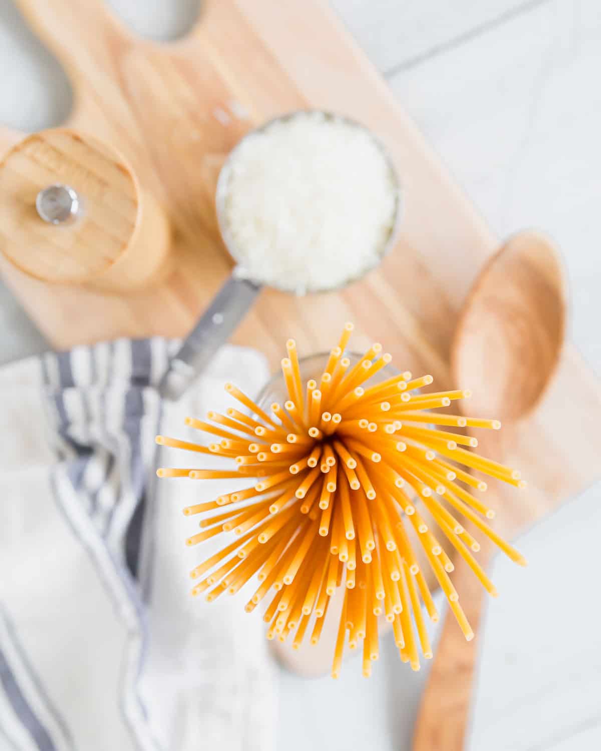 Bucatini standing in a jar with cheese and pepper in the background.