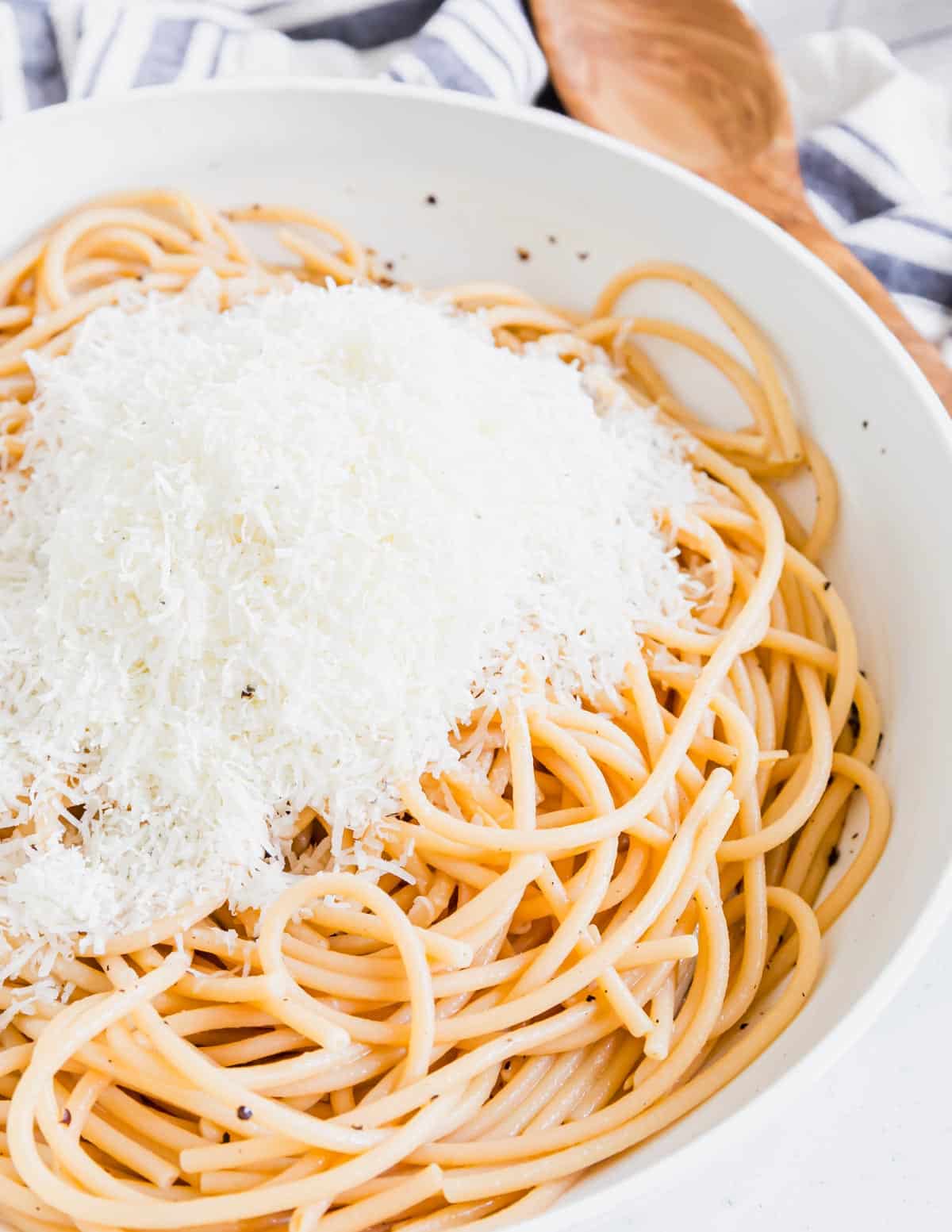 Cooked bucatini in a white pan with pecorino romano cheese on top.