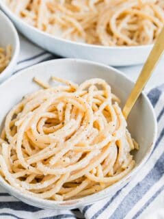 Close up of bucatini cacio e pepper twirled into a small serving bowl with a fork.