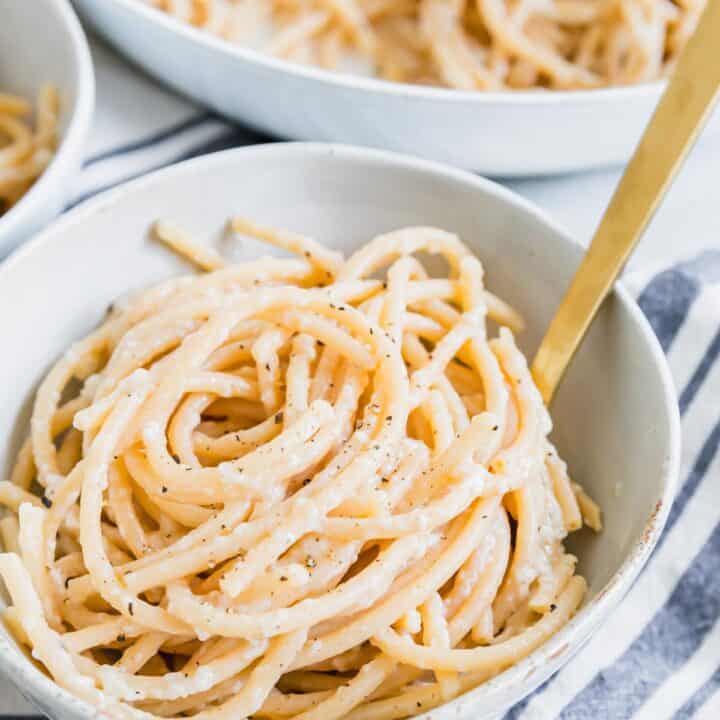 Close up of bucatini cacio e pepper twirled into a small serving bowl with a fork.