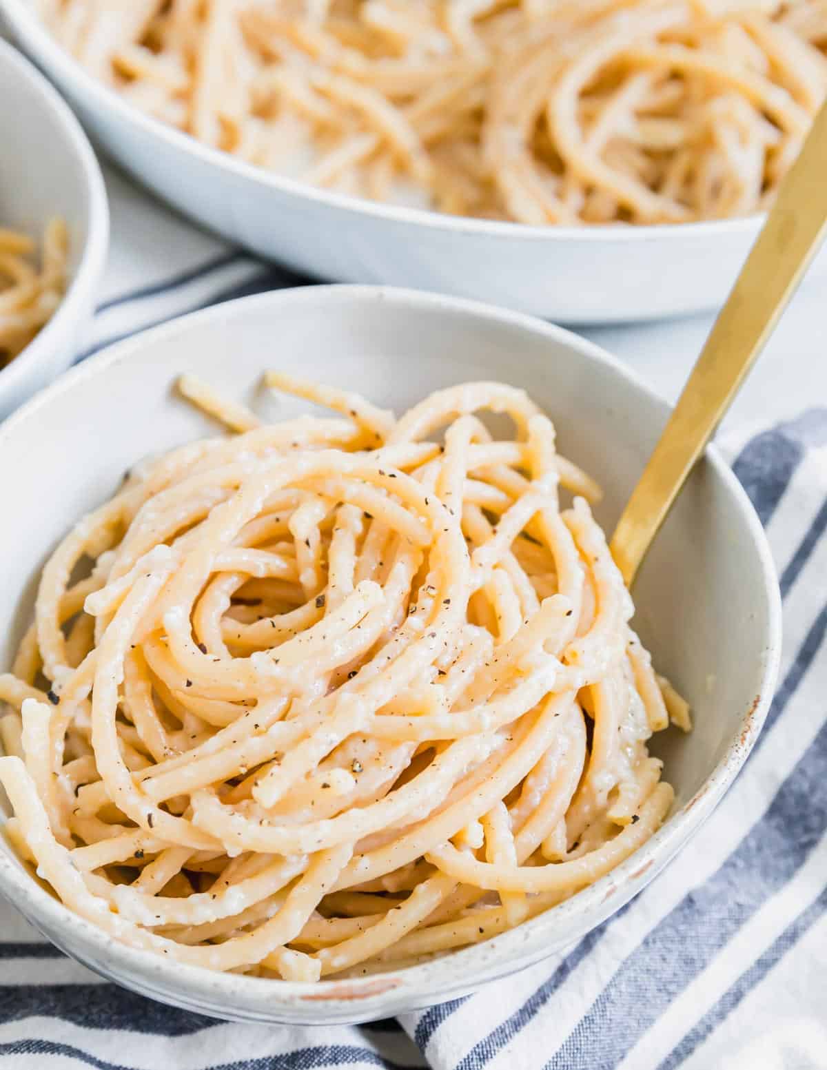 Close up of bucatini cacio e pepper twirled into a small serving bowl with a fork.