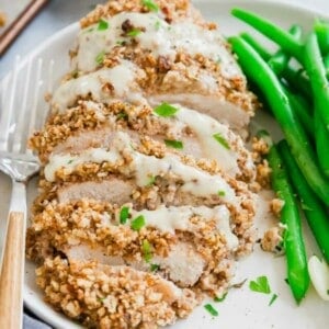 Close up of pecan chicken sliced on a plate served with green beans with a fork on the side.