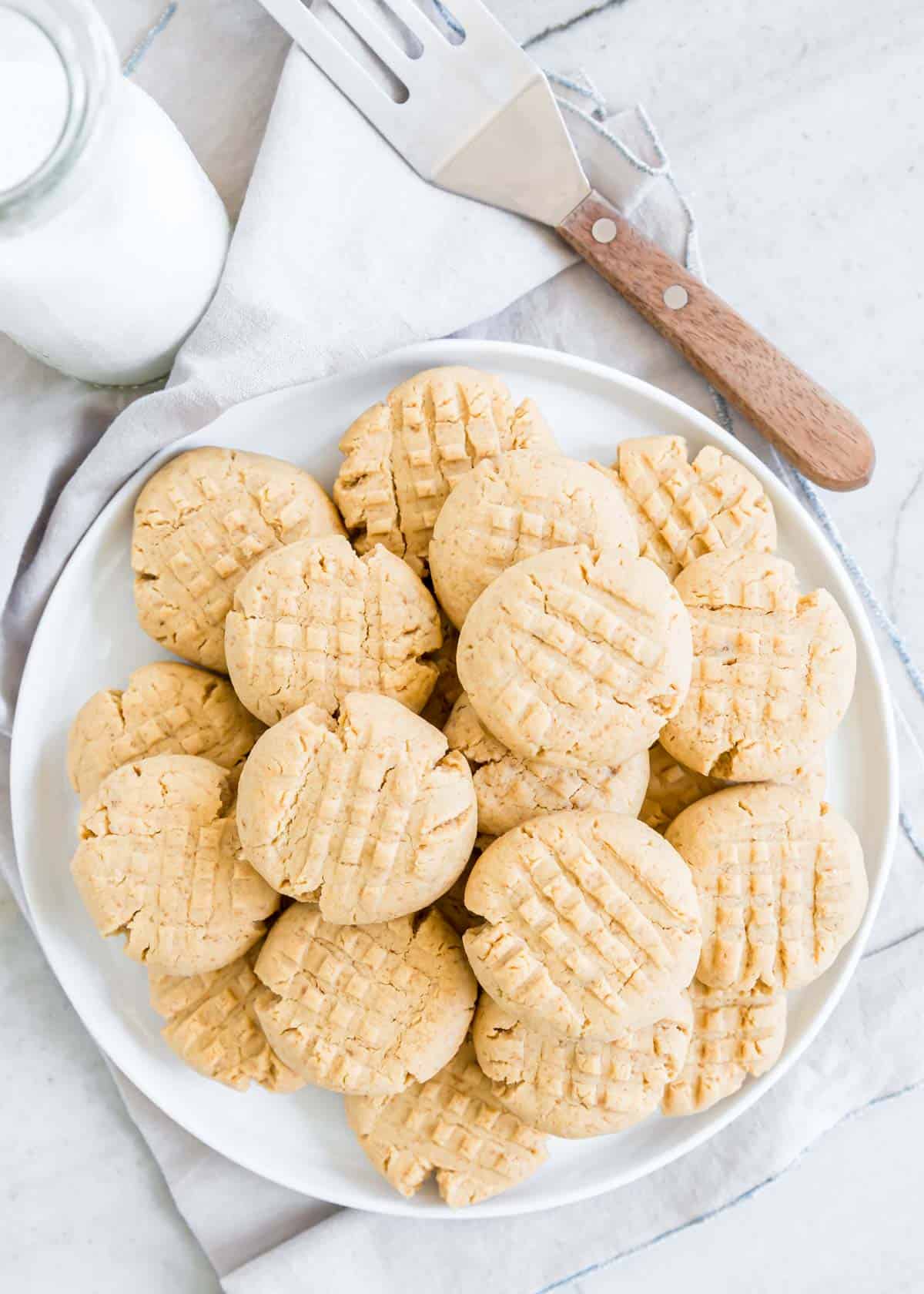 Gluten free peanut butter cookies on a white plate with milk and spatula on the side.