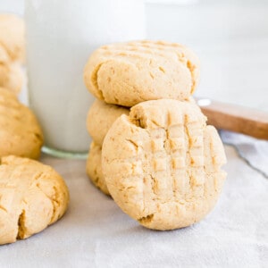 Close up of a gluten-free peanut butter cookie standing against a stack of cookies with milk.