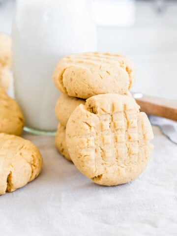 Close up of a gluten-free peanut butter cookie standing against a stack of cookies with milk.