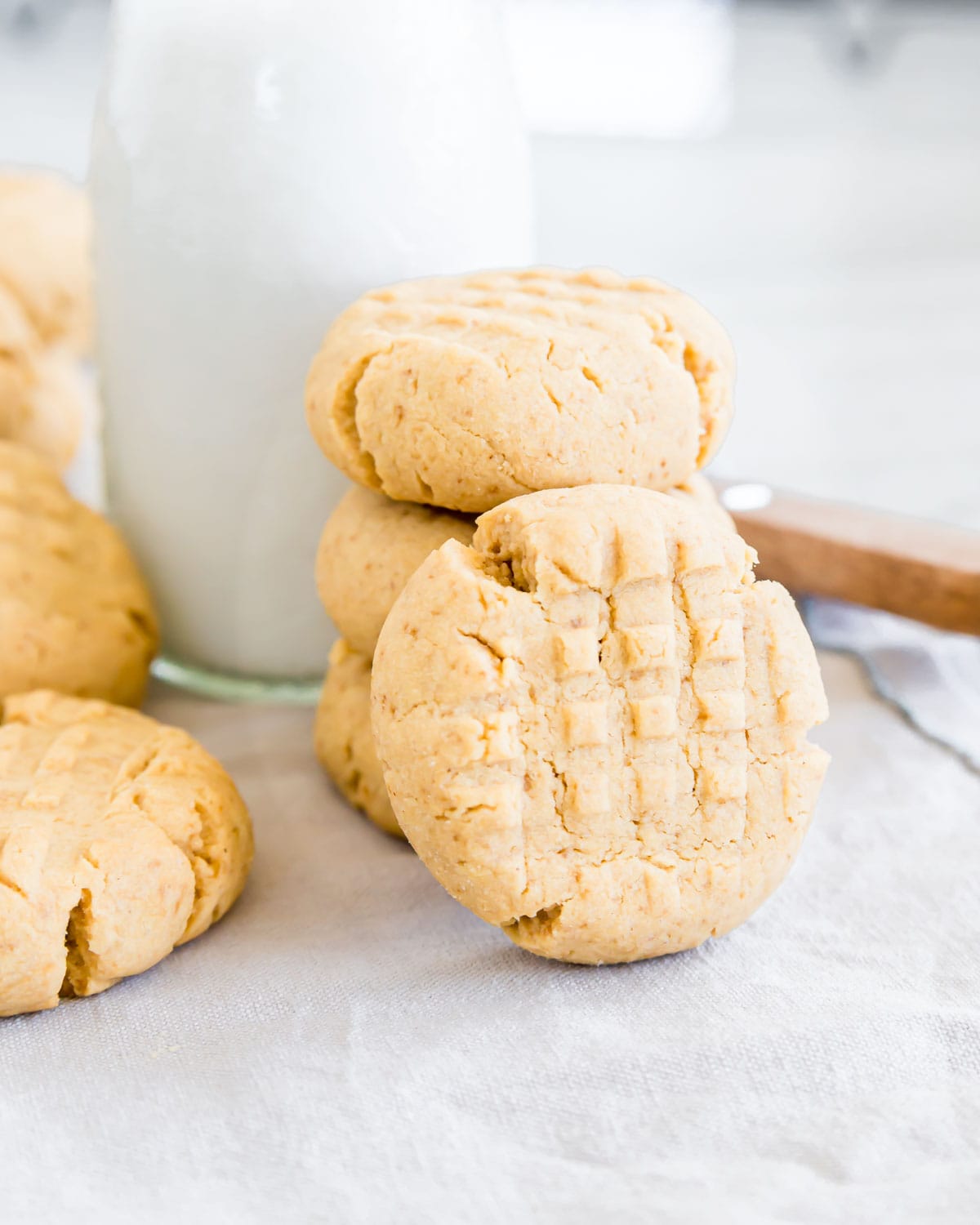 Close up of a gluten-free peanut butter cookie standing against a stack of cookies with milk.