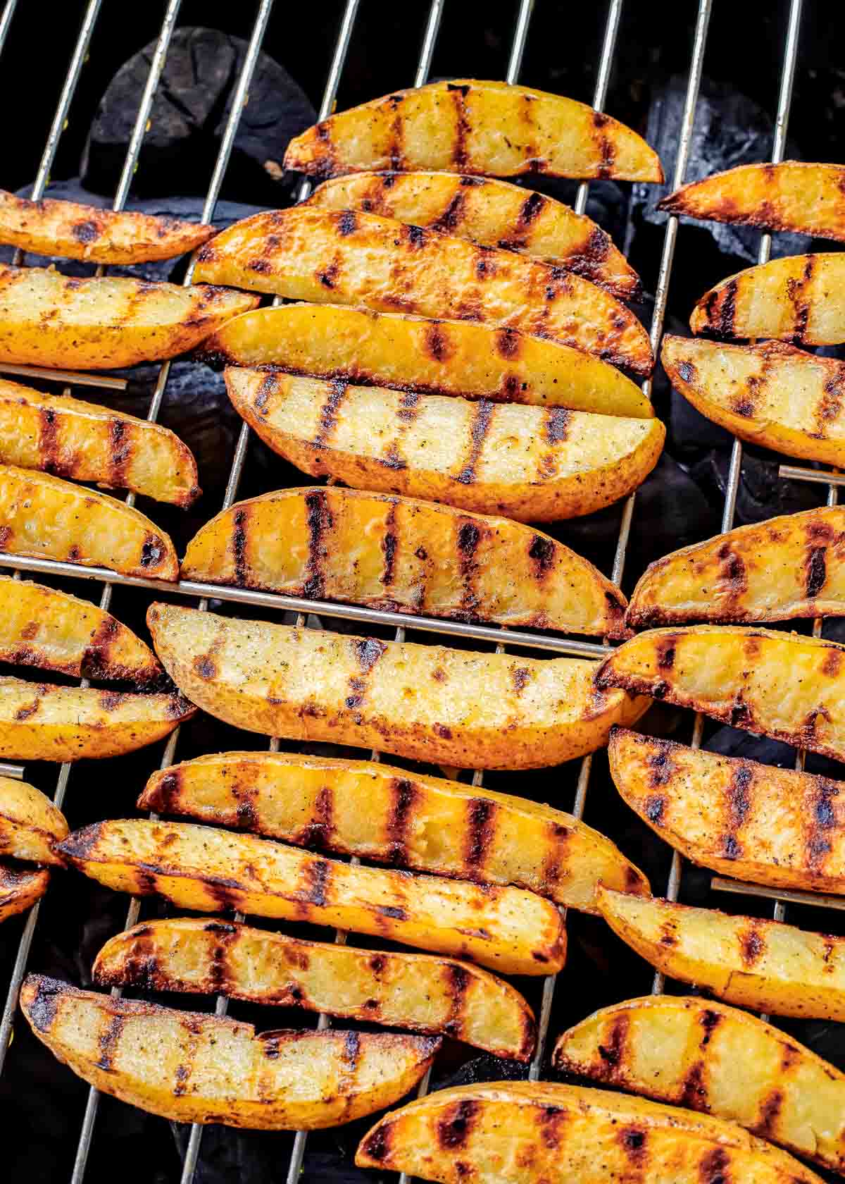 Grilled potato wedges on grill grates.