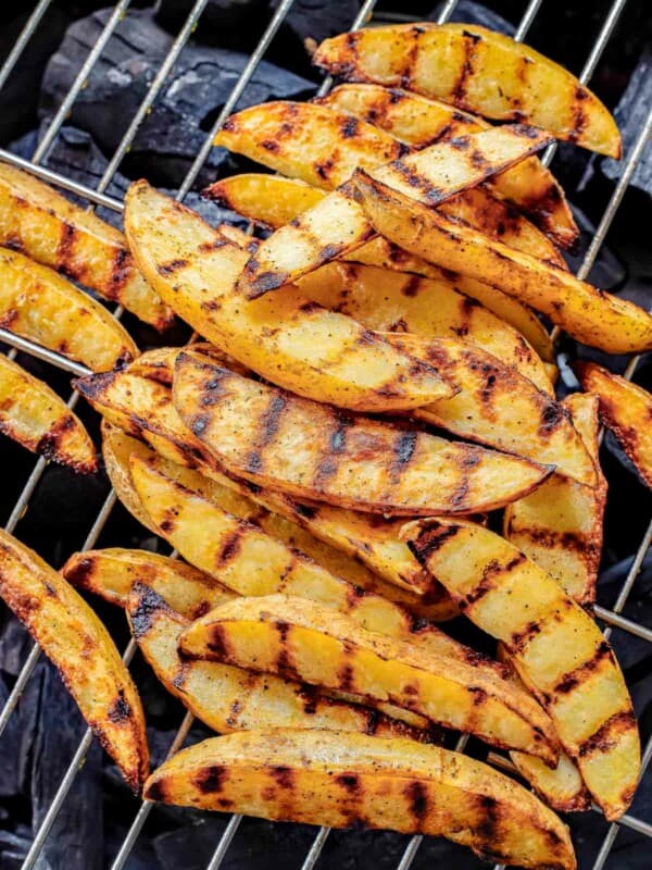Grilled potato wedges in a pile on a charcoal grill.