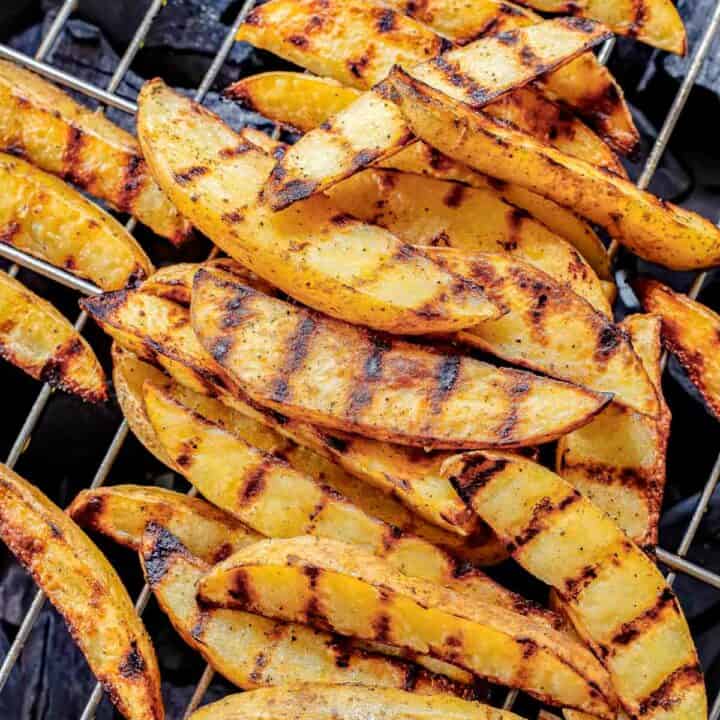 Grilled potato wedges in a pile on a charcoal grill.