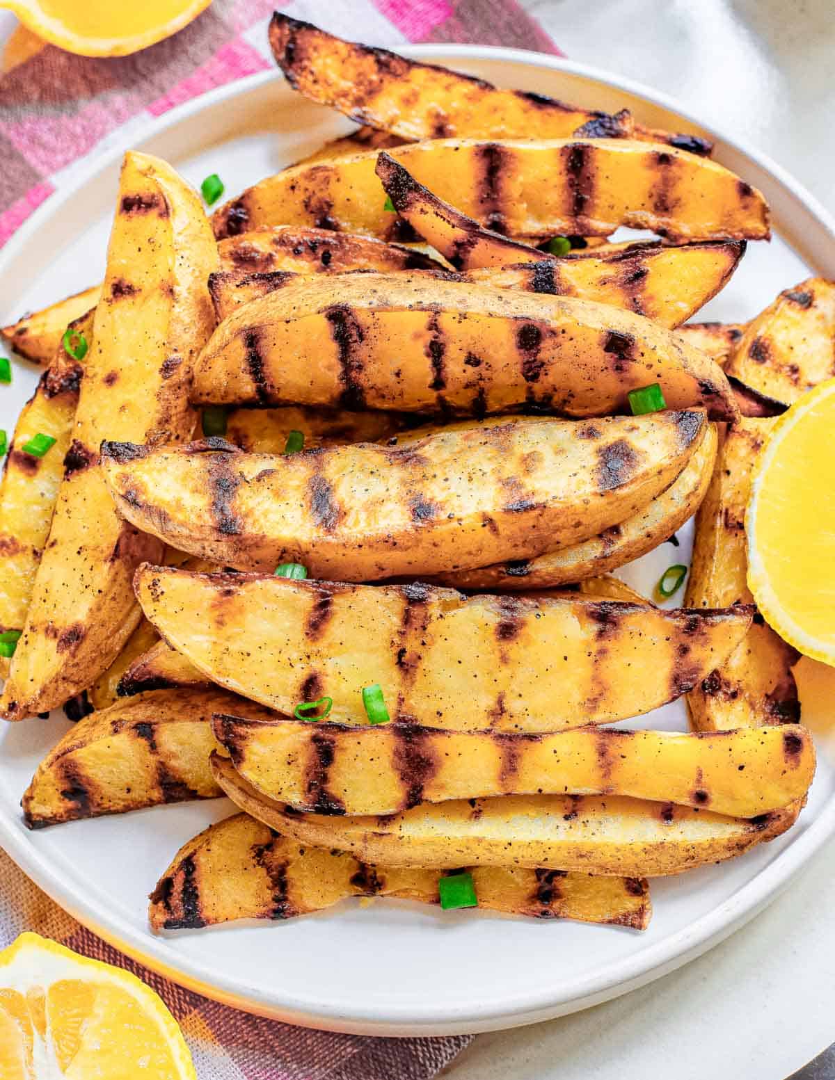 Seasoned grilled potato wedges on a white plate.