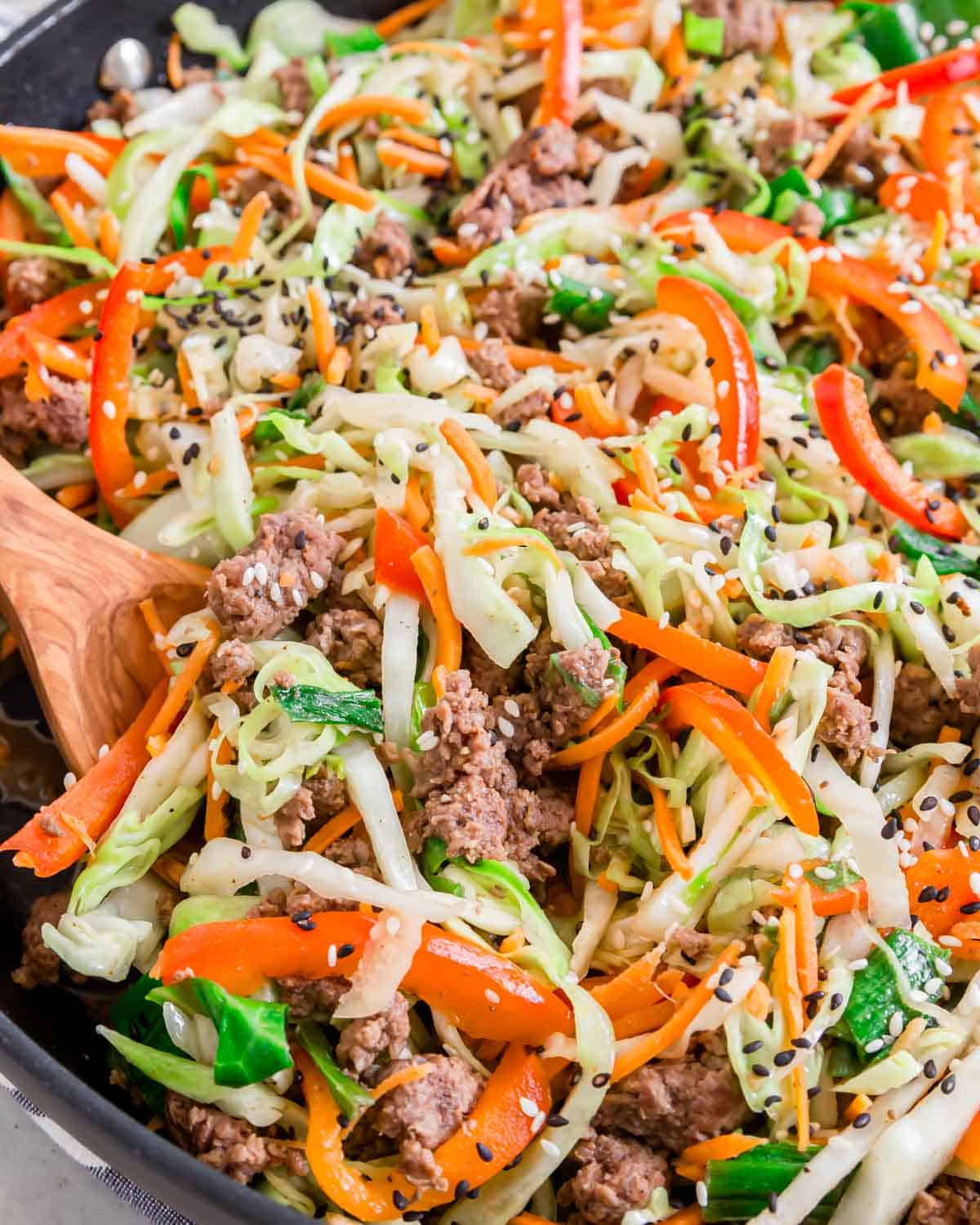 Close up shot of ground beef cabbage stir fry in a saute pan with a wooden serving spoon.