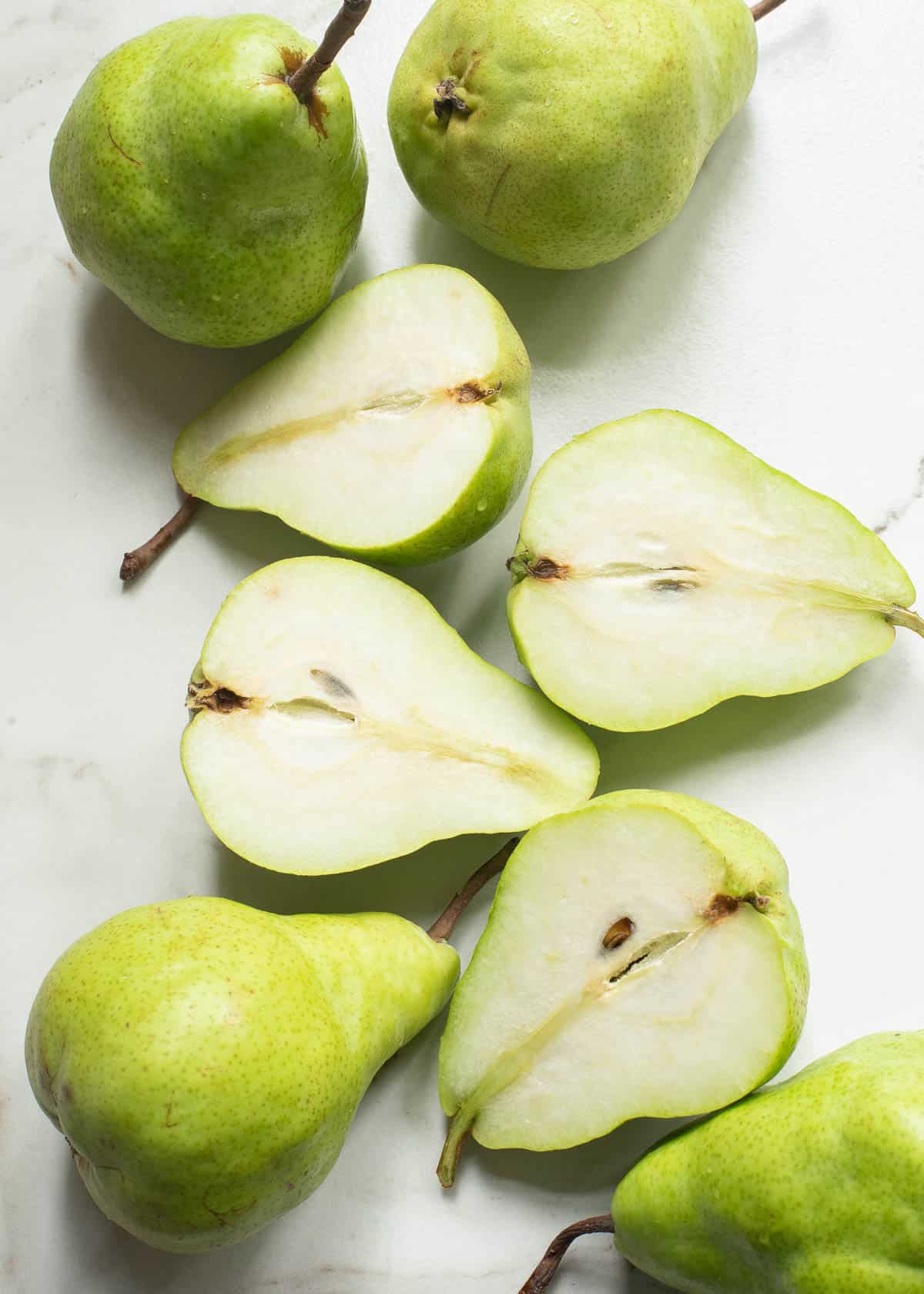 Green pears cut in half on a white surface.