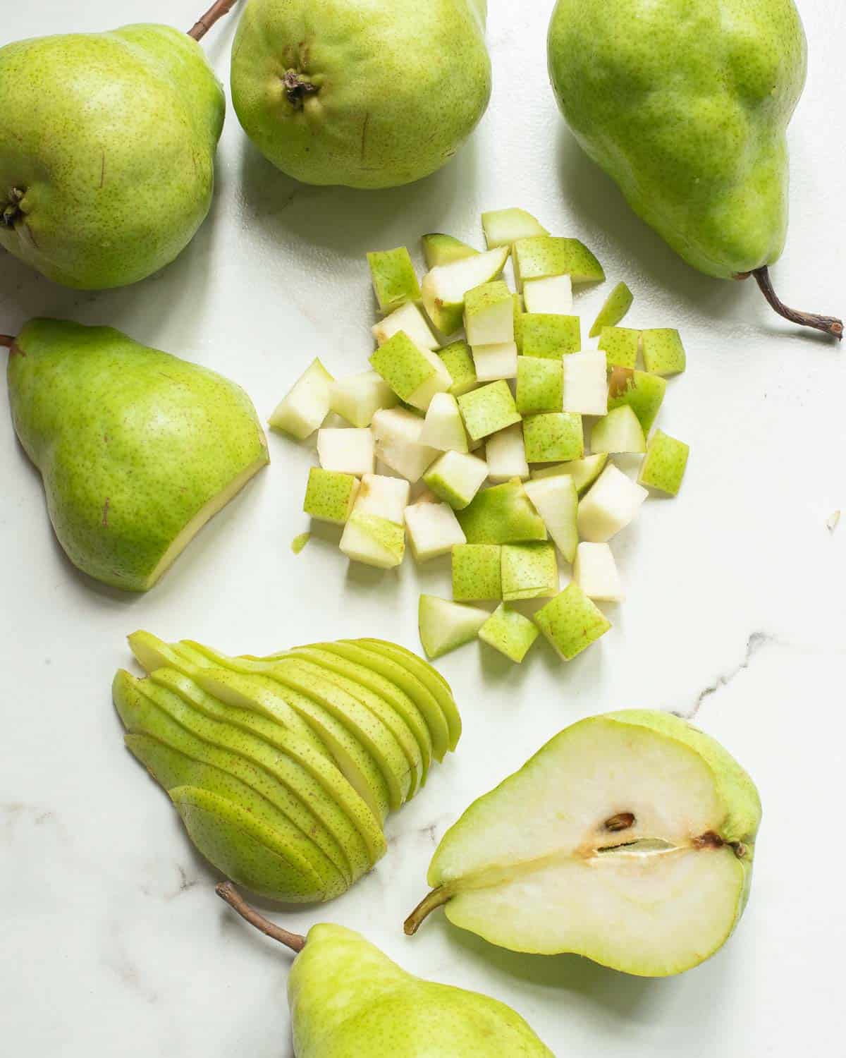 Chopped, sliced and halved pears on a white surface.