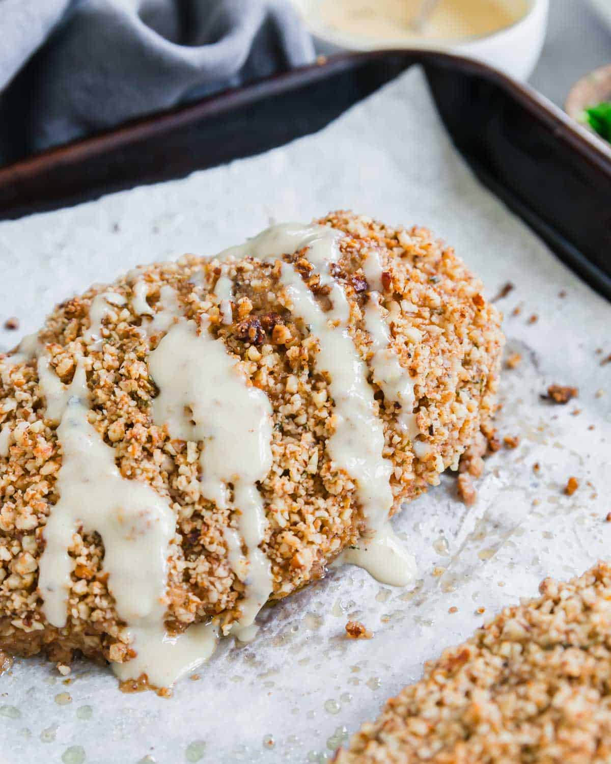 Pecan crusted chicken drizzled with a yogurt honey dijon sauce on a baking sheet lined with parchment paper.