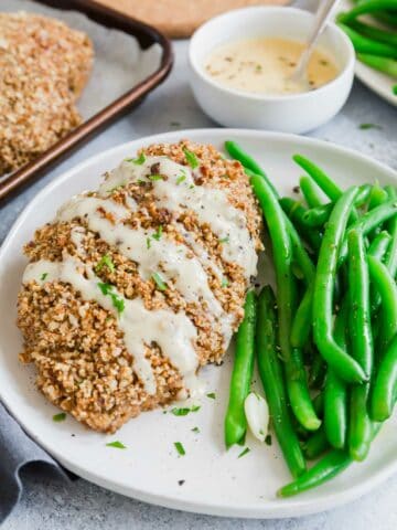 Pecan crusted chicken with honey dijon sauce drizzled on top on a plate.
