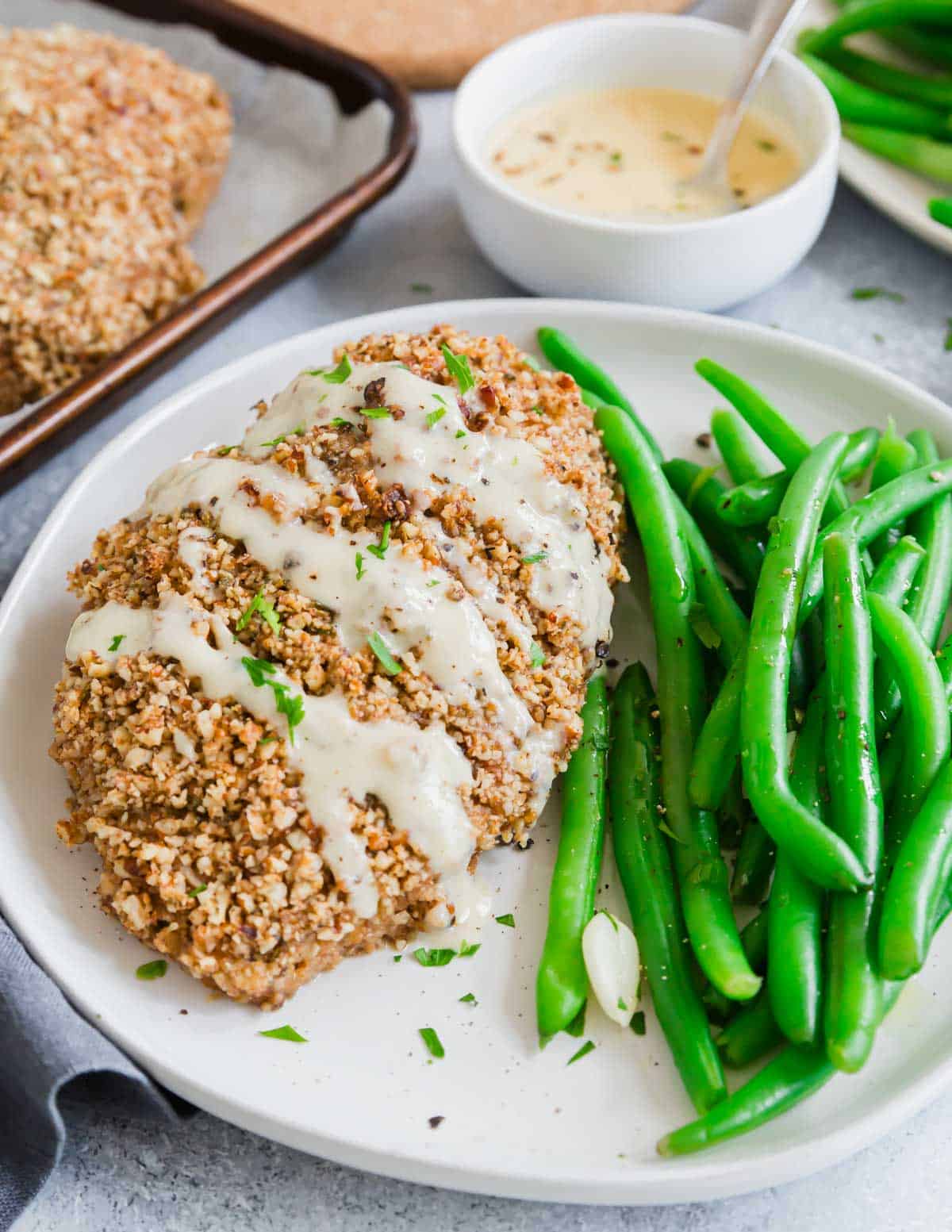 Pecan crusted chicken with honey dijon sauce drizzled on top on a plate.