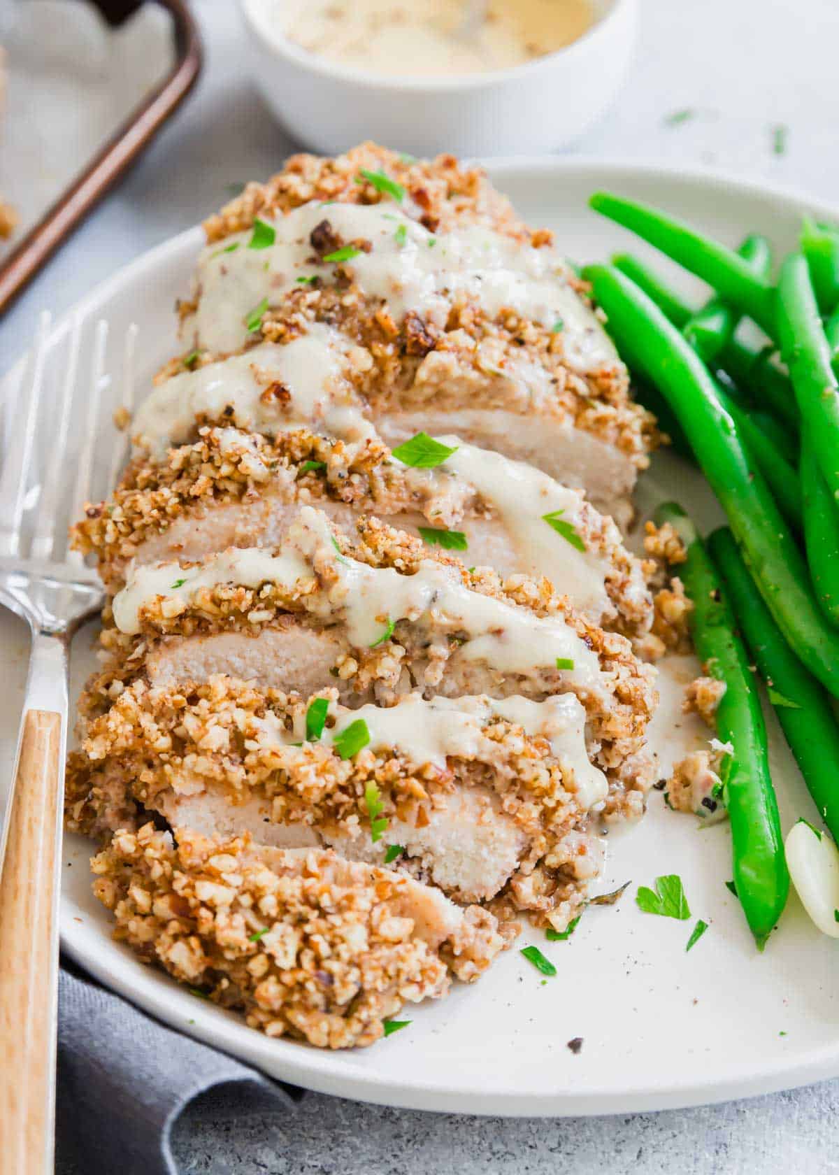 Close up of pecan chicken sliced on a plate served with green beans with a fork on the side.