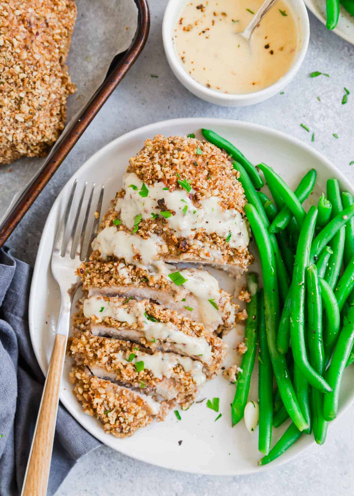 Sliced pecan chicken on a plate with green beans and a fork.