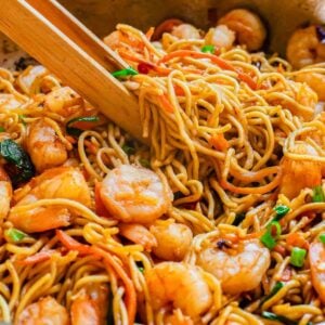 Shrimp lo mein recipe with wooden tongs in a skillet.