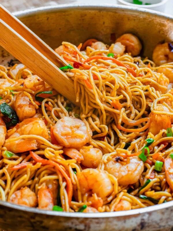 Shrimp lo mein recipe with wooden tongs in a skillet.