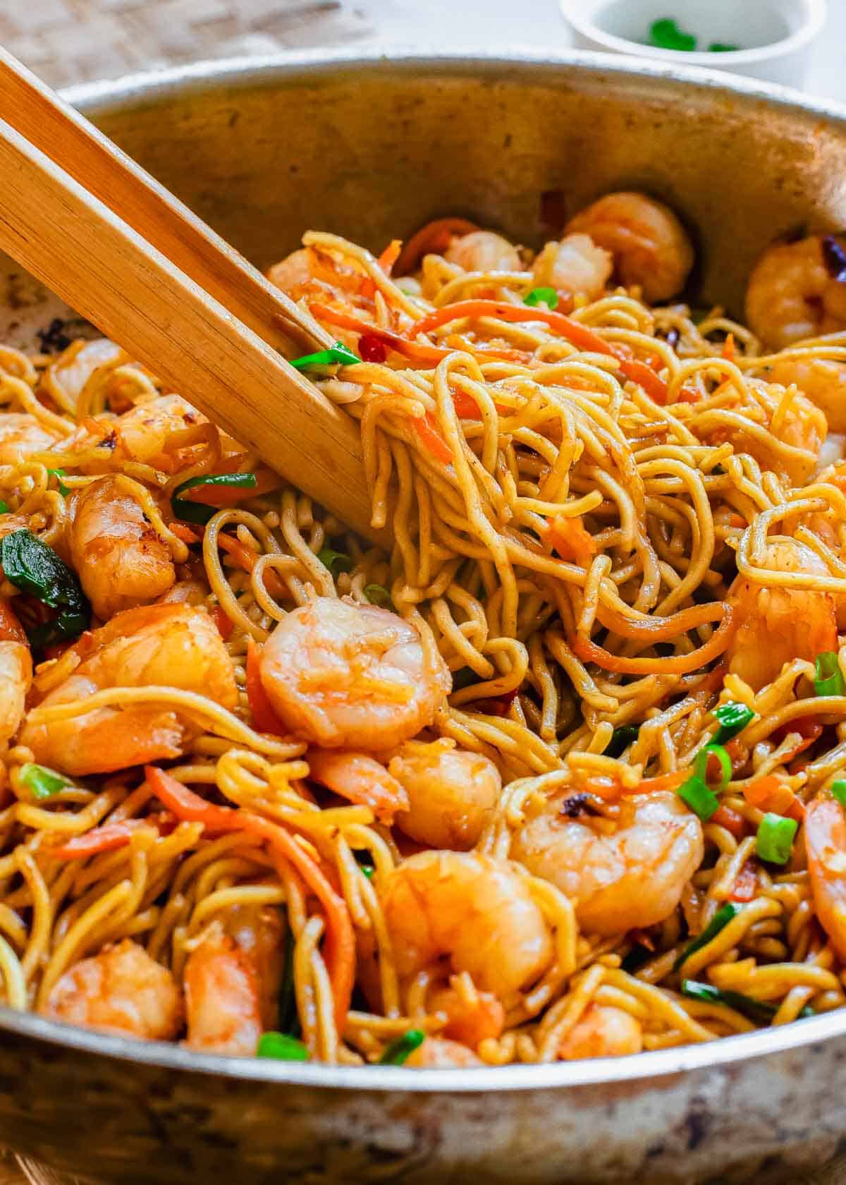 Shrimp lo mein recipe with wooden tongs in a skillet.