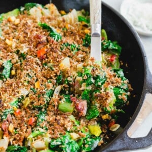 A skillet full of escarole with breadcrumbs and cheese on top with a serving spoon.