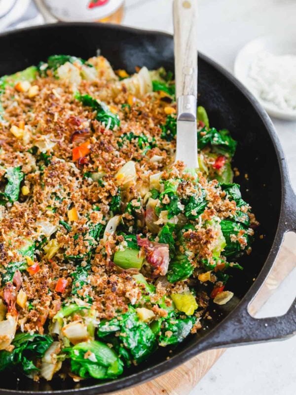 A skillet full of escarole with breadcrumbs and cheese on top with a serving spoon.