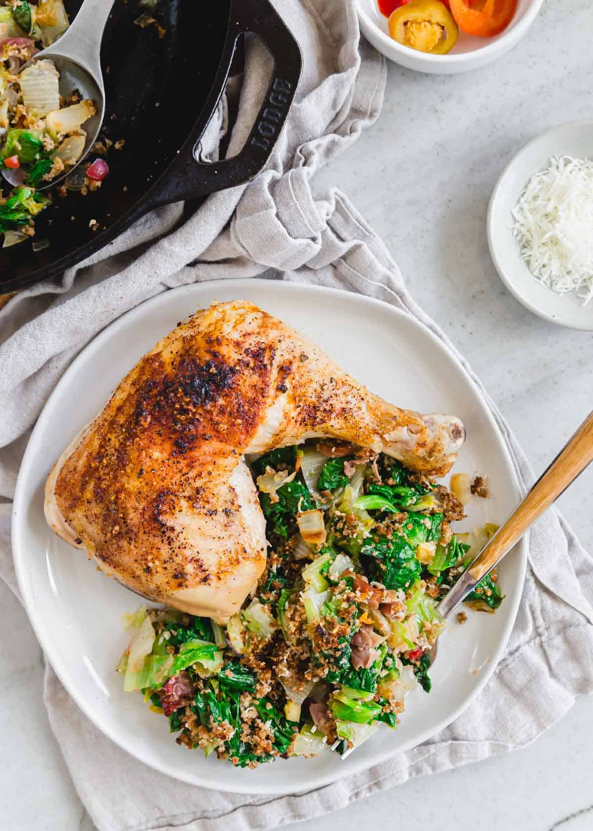 A white plate with chicken and Utica greens recipe on the side with a fork.