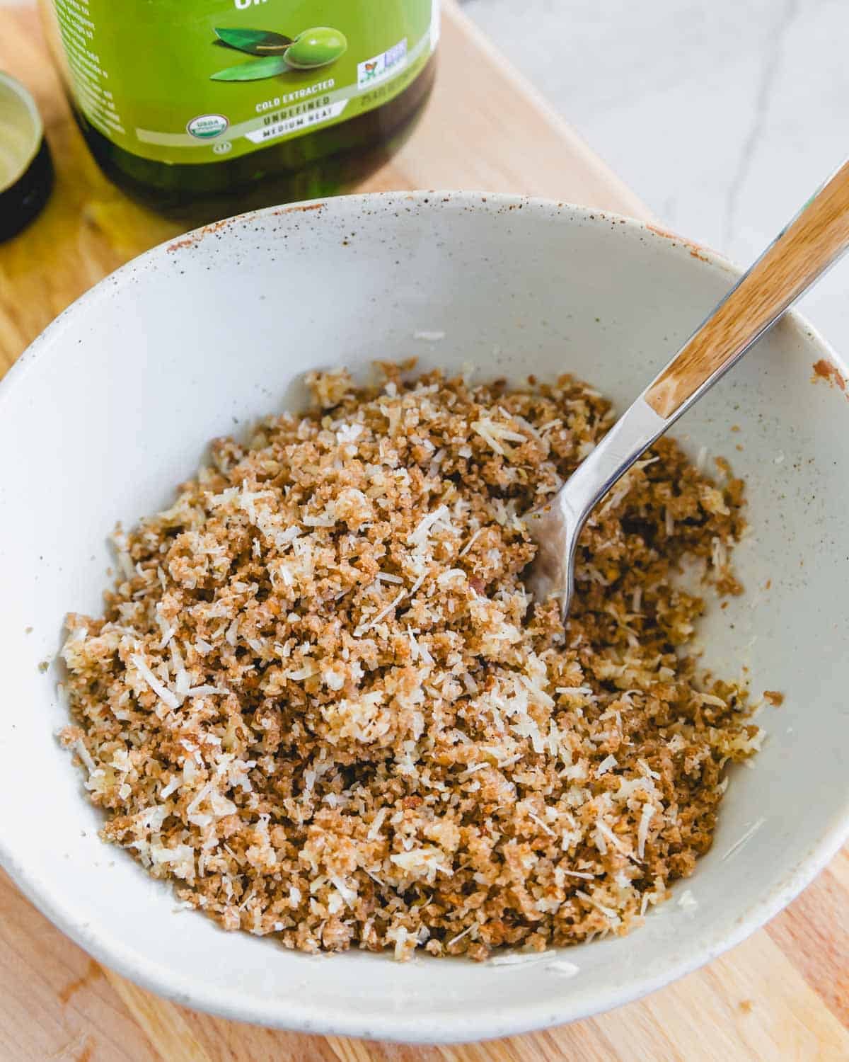 A bowl with breadcrumbs, cheese, spices and olive oil with a fork.