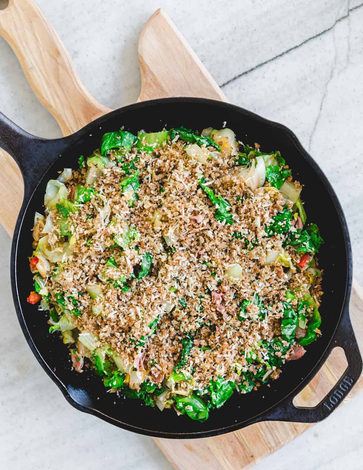 Utica greens topped with breadcrumb mixture before broiling in a cast iron skillet.