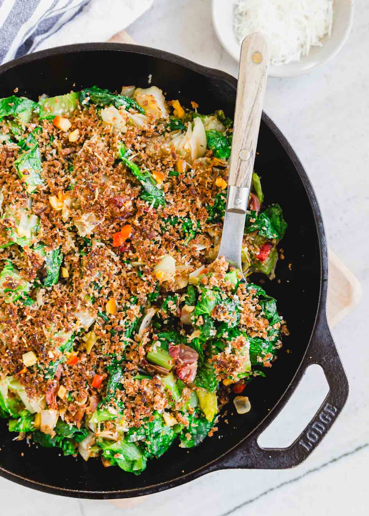 A serving spoon scooping Utica greens out of a cast iron skillet.