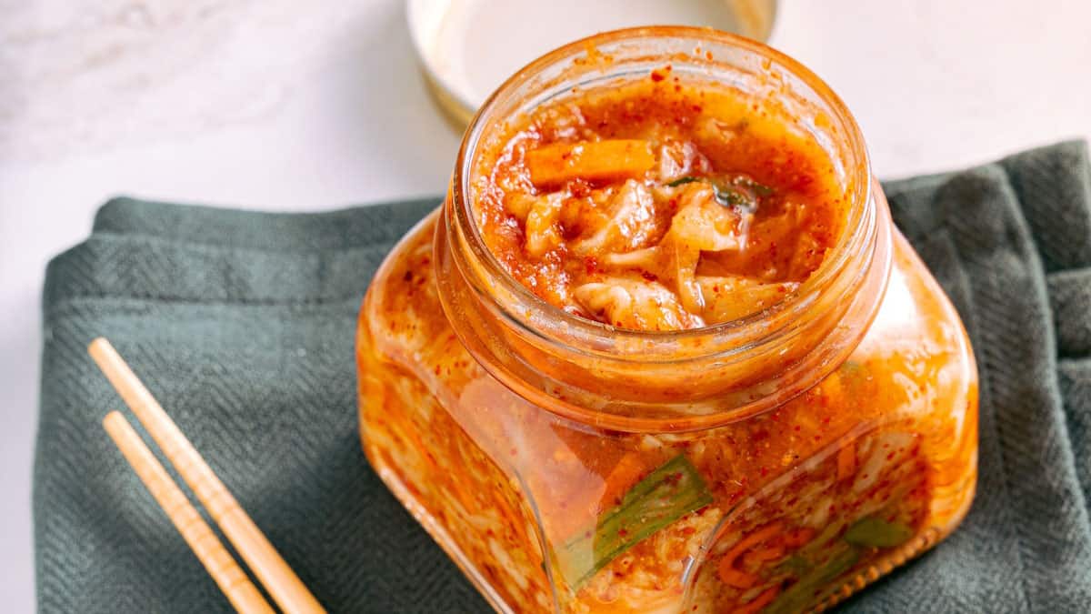 A jar of kimchi with chopsticks on a table.