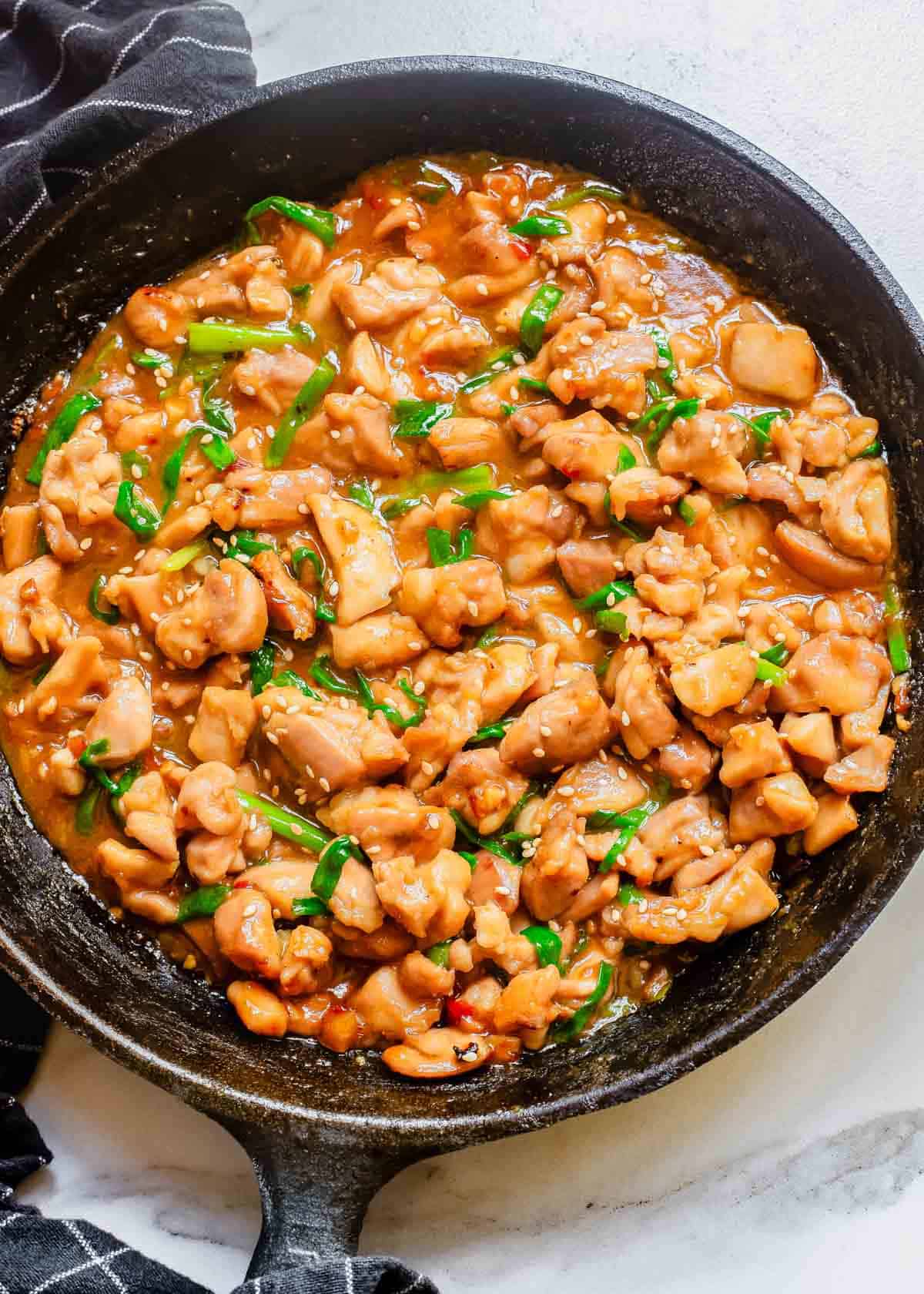 A skillet filled with chicken thigh pieces in a gochujang sauce.