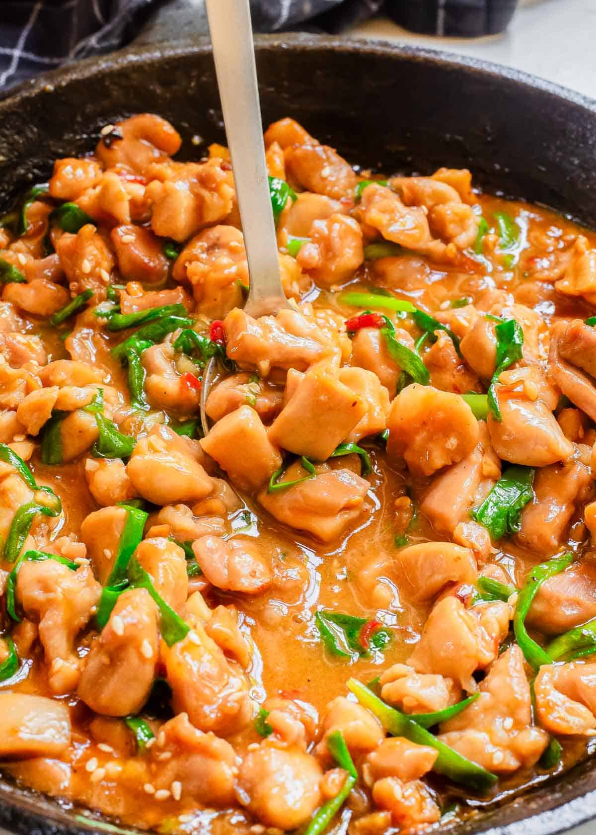 Gochujang chicken with green onions in a skillet with a serving spoon.