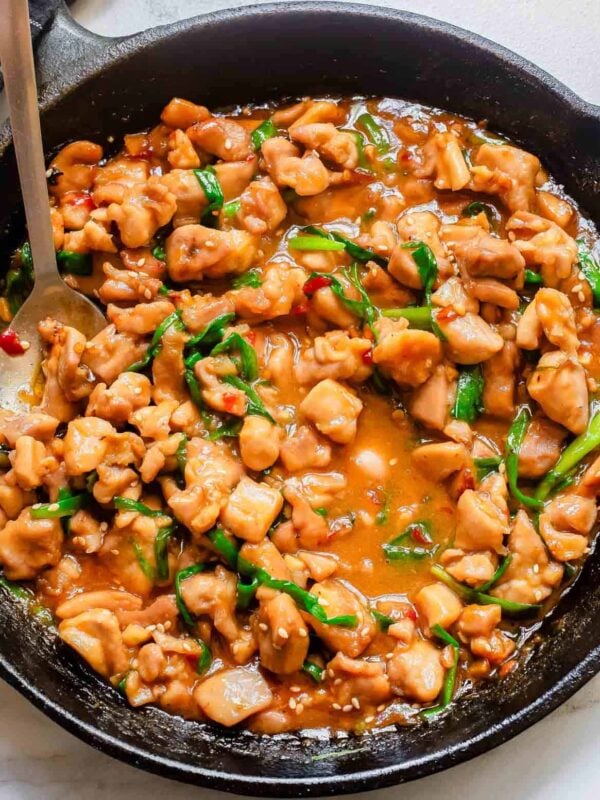 Chinese gochujang chicken in a cast iron skillet with a metal serving spoon.